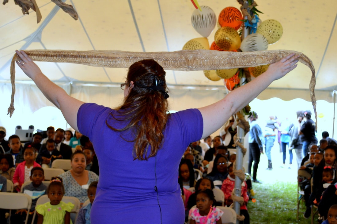 A large crowd appears engaged as a presenter holds a long snake skin above her head